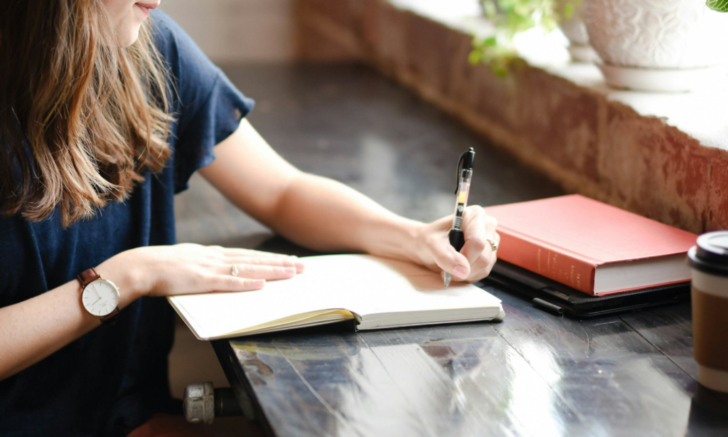 woman is writing in a notebook to practice self-compassion