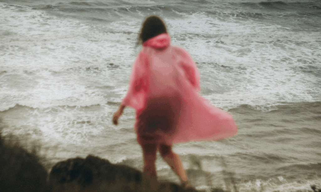 woman walks by the coast line in the wind and rain and feels overwhelmed by life