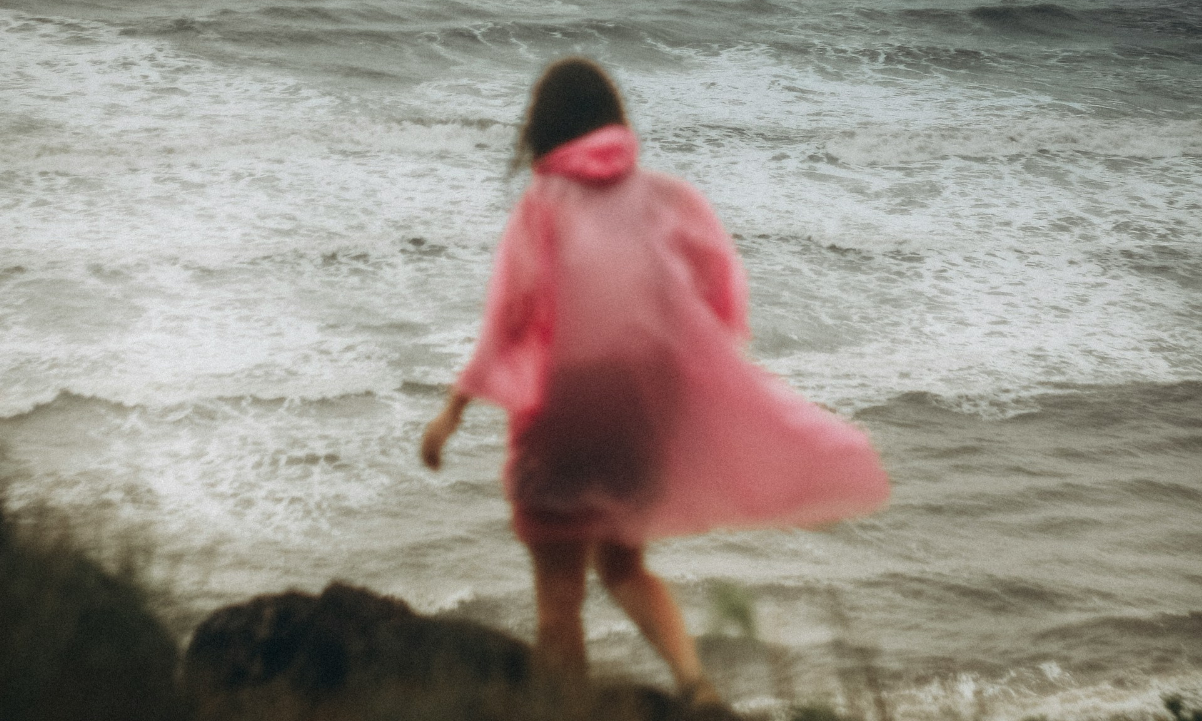 woman walks by the coast line in the wind and rain and feels overwhelmed by life