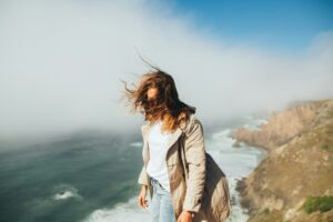 A woman standing on a cliff above the ocean, wind in her hair