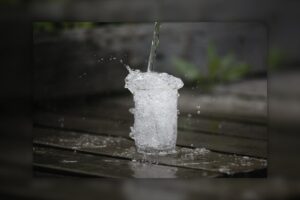 water being poured into an already overflowing glass on a wooden table