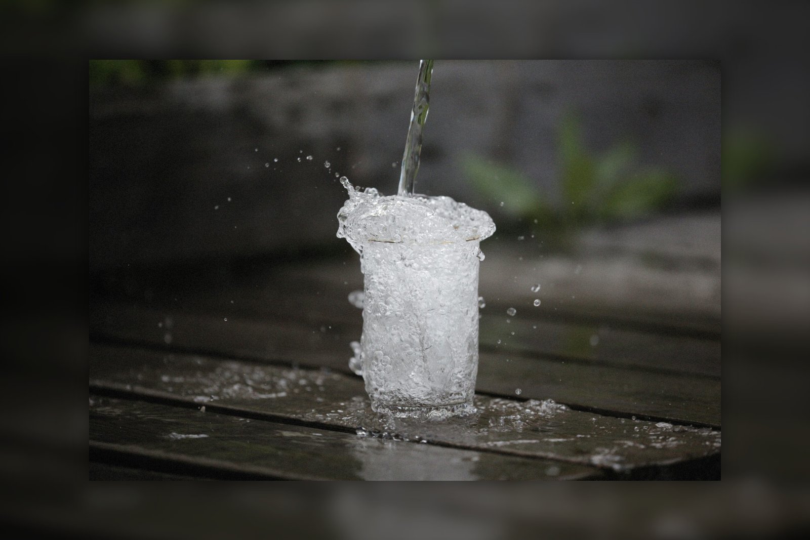water being poured into an already overflowing glass on a wooden table